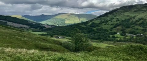 Lush green valley between mountains in Scotland, with the sun breaking through the clouds