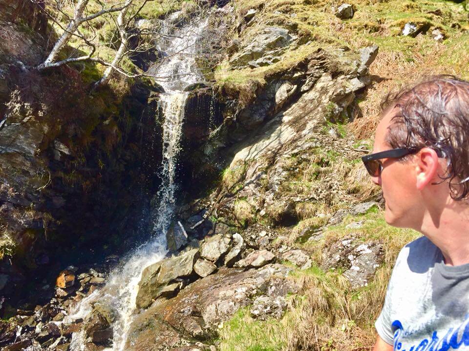 Man looks at waterfall. He is wet as he has been behind the waterfall.