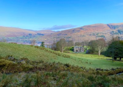 open vale with a Scottish manor house in the background and a lake and hills beyond