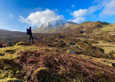 a man with a hiking backpack in the Scottish Highlands climbing up to a snow capped mountain peak