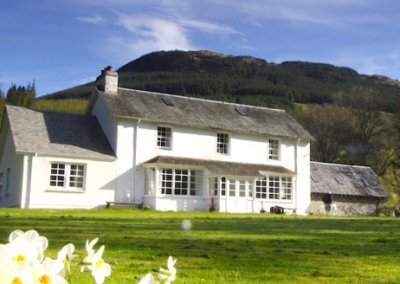 19th century white house with a green field in front and mountains behind