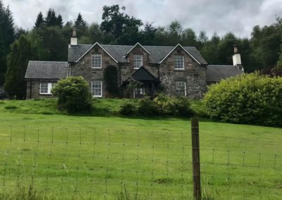 18th century stone house with a green field in front and trees behind