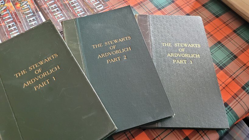 three hardcover books spread on a red tartan table cloth