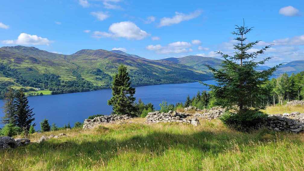 View of a Highland Scottish loch from up on a hillside on a sunny day. The water is crisp blue.