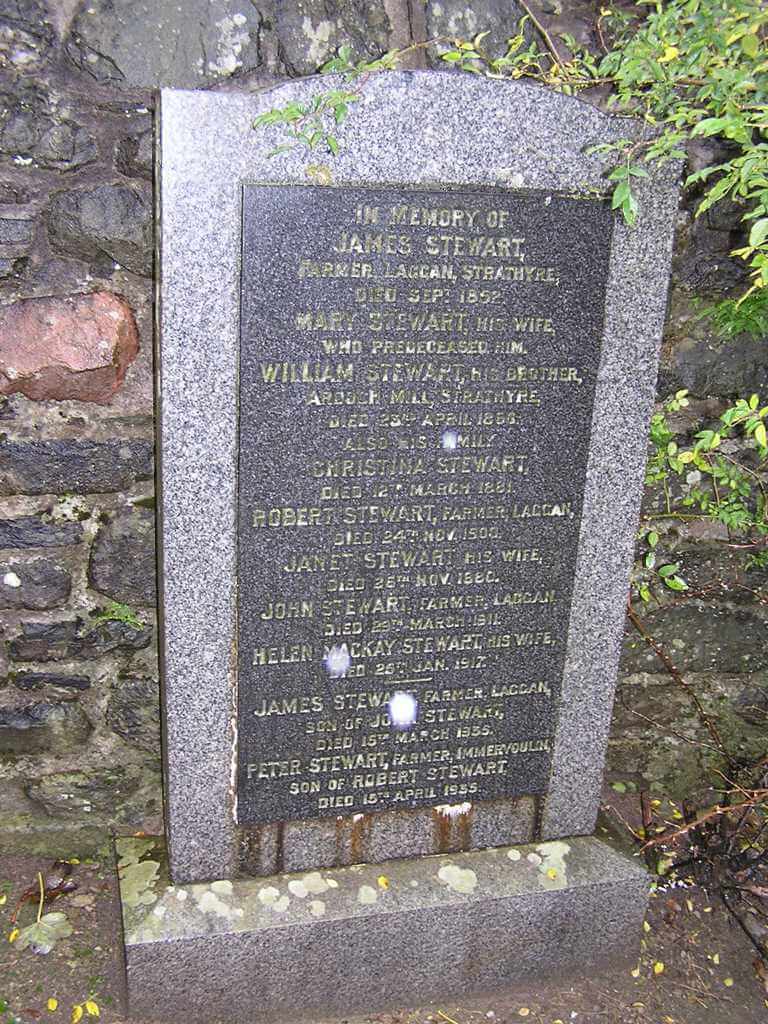 granite gravestone against a stone wall, inscribed with multiple generations