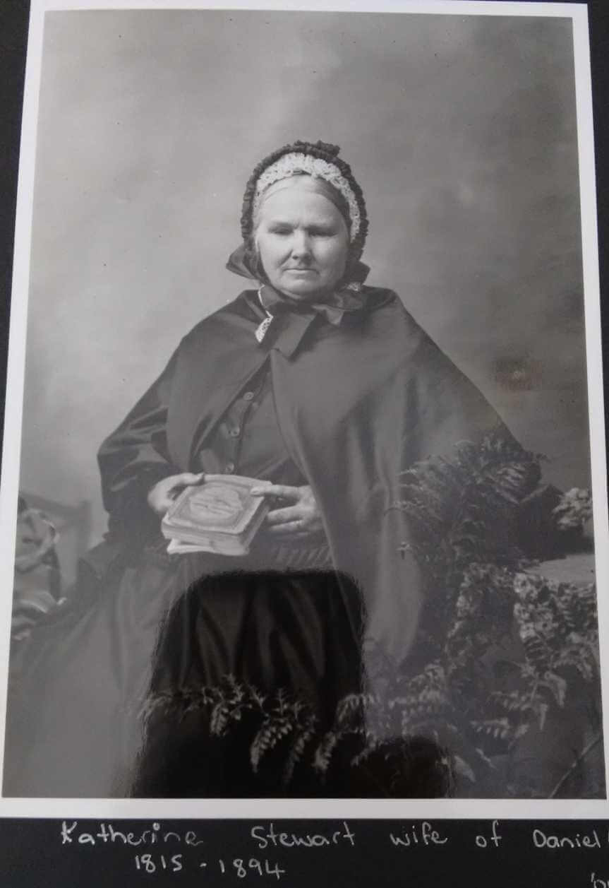 Elderly woman wearing a cape and hood posing in a portrait studio ca. 1890s