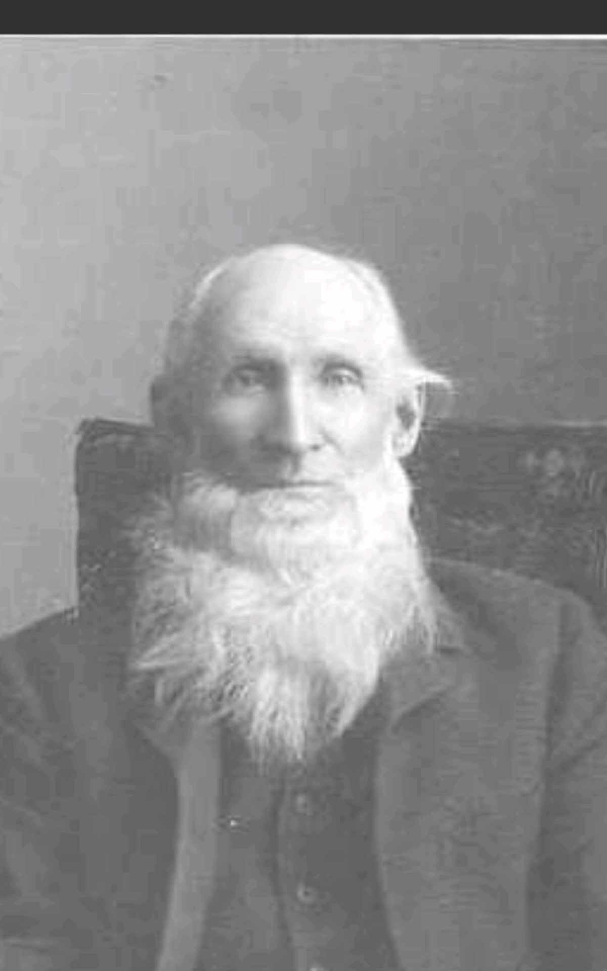 elderly man in his 70s posing seated for a studio portrait ca, 1910. He has thin white hair on top and a full, bushy, white beard down to his chest.