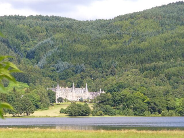 A large, elegant, 19th-century hotel overlooking a lake with tree-covered mountains behind