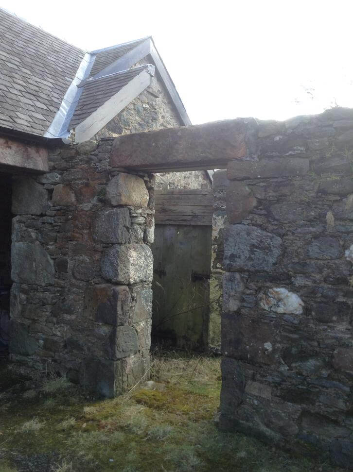 stone walls and doorway of an old Scottish farm building. There is no roof and the floor is overgrown with long grass.